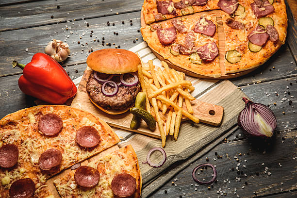 pizza and hamburger on wooden background with French fries red onion garlic and sweet pepper and pickles